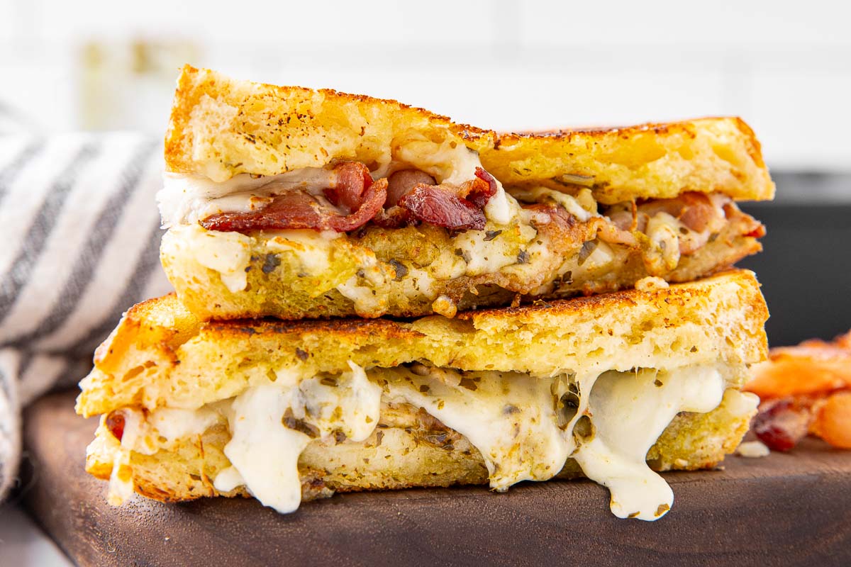A pesto grilled cheese sandwich sliced in half and stacked on a cutting board to show the filling inside.