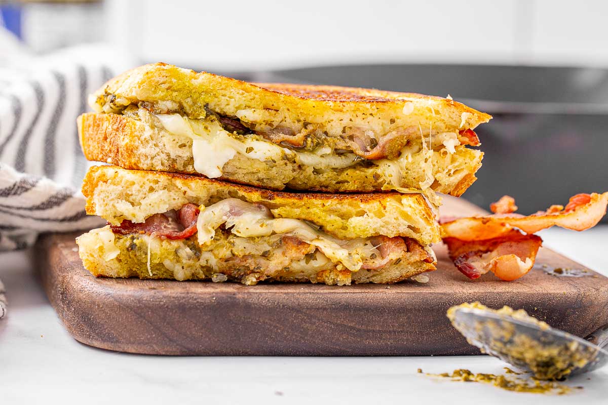 A pesto grilled cheese sandwich sliced in half and stacked on a cutting board to show the filling inside.