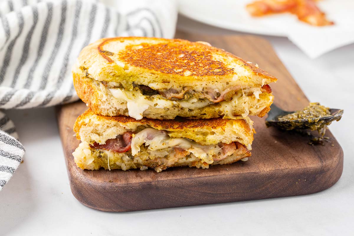 A pesto grilled cheese sandwich sliced in half and stacked on a cutting board to show the filling inside.