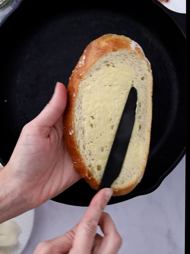 Hands using a knife to spread butter on a piece of bread for a pesto grilled cheese sandwich.