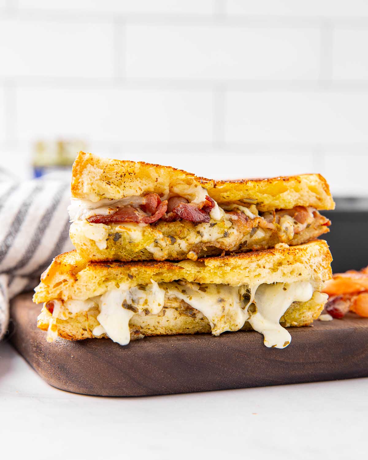 A pesto grilled cheese sandwich sliced in half and stacked on a cutting board to show the filling inside.