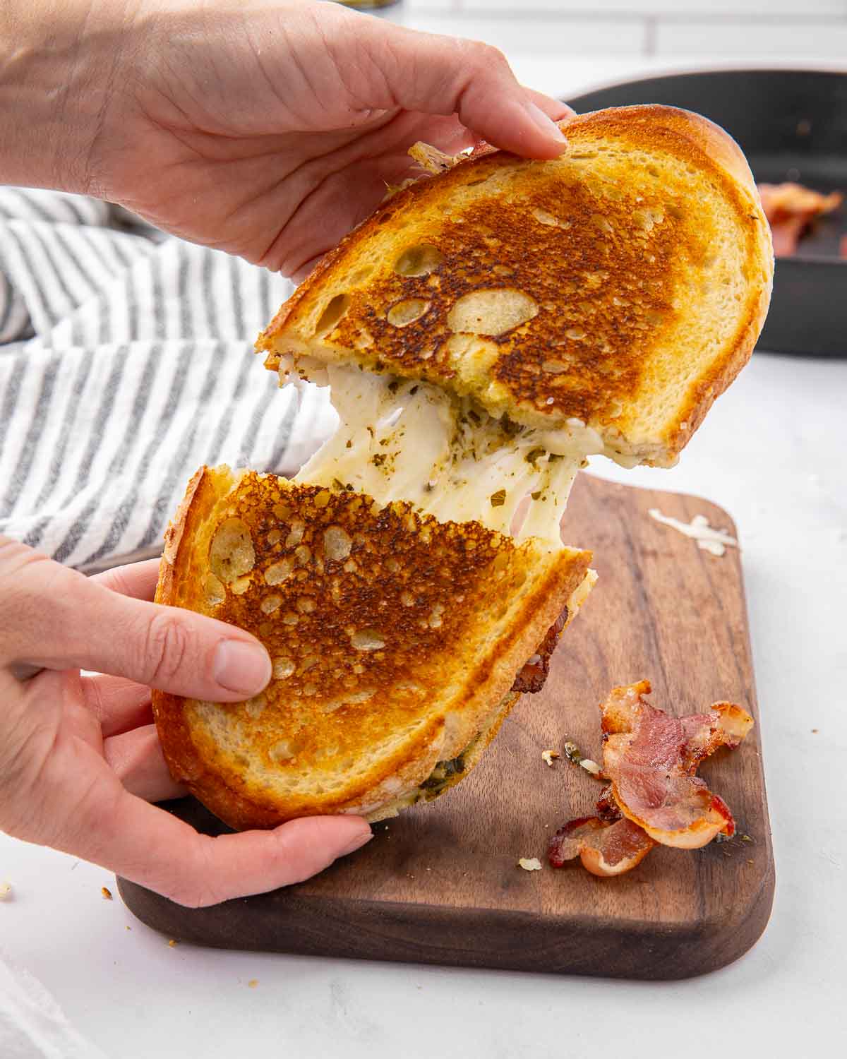 Hands pulling a pesto grilled cheese in half to show melted cheese in the middle.