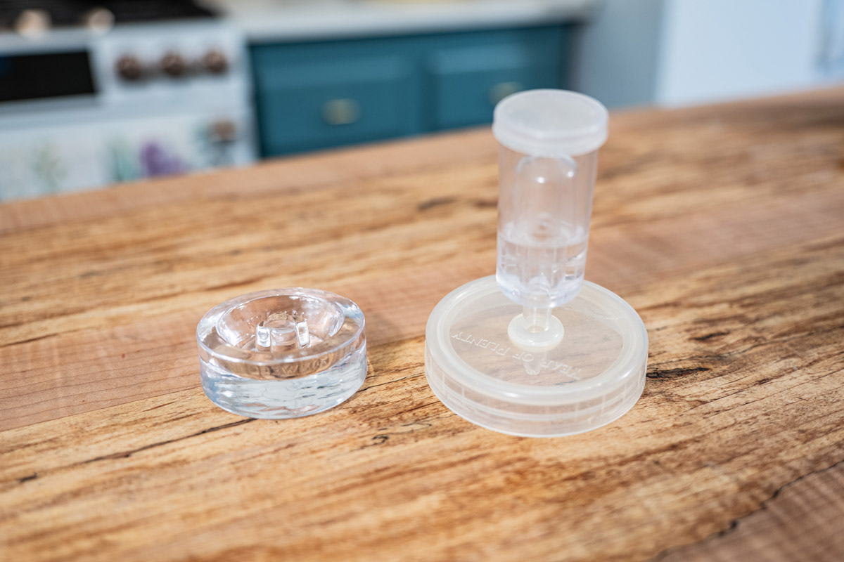 A fermenting glass weight and an airlock lid on a counter.