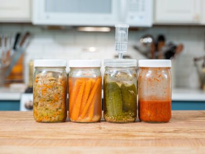 Four jars of fermented foods on a kitchen counter.